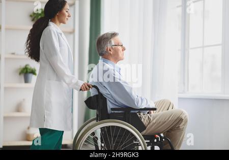 Junge Ärztin hilft älteren Mann im Rollstuhl in Innenräumen, Platz kopieren Stockfoto