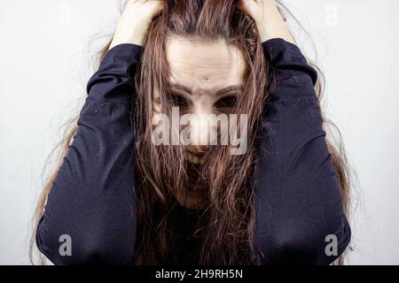 Gestresste, verängstigte und schreiende junge verrückte Frau in Schwarz vor hellem Hintergrund. Stockfoto
