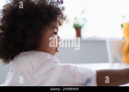Seitenansicht eines lockigen afroamerikanischen Mädchens zu Hause, verschwommener Vordergrund Stockfoto