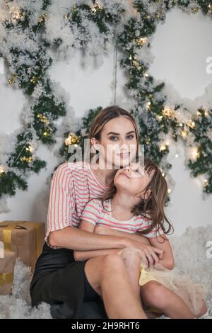 Weihnachts-Studio-Familiendreh. Neujahrsfoto der glücklichen Familie. Schöne Mutter und nette Tochter umarmen einander und lächeln Stockfoto