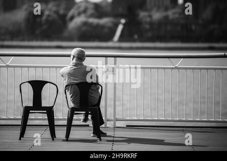 Ein alter Mann wartet auf seine Frau, während er am huangpu-Fluss sitzt, im Sommer in Shanghai Stockfoto
