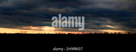 Sonnenstrahlen durchbrechen die Wolkendecke in einer Panoramaaufnahme mit Hintergrundbeleuchtung. Stockfoto