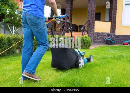 Ein Mann mäht einen Rasen mit einem elektrischen Mäher im Garten Hinterhof. Stockfoto