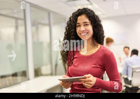 Lächelnde junge Frau als Auszubildende oder Studentin mit Tablet-Computer im Büro Stockfoto