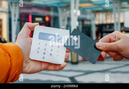 Nicht erkennbare weibliche Kundin mit Plastikkarte beschneiden, die NFC-Kauf am POS-Terminal im Geschäft in der Stadt macht Stockfoto