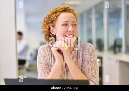 Junge Geschäftsfrau sitzt zufrieden am Computer im Büro Stockfoto