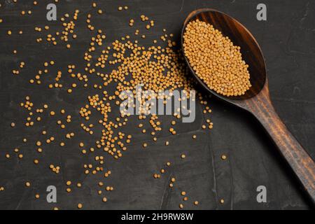 Yellow Raw Organic Senf Seeds auf Holzlöffel auf dunklem Beton Hintergrund Stockfoto