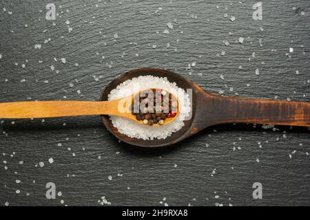 Meersalz und Pfefferkörner auf Holzlöffeln auf Schiefergrund. Flach liegend. Minimalistischer Style. Stockfoto