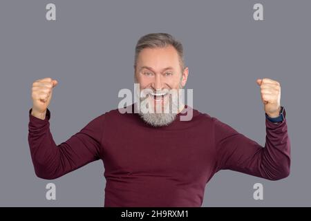 Reifer Mann im burgunderroten Hemd sieht positiv aus Stockfoto