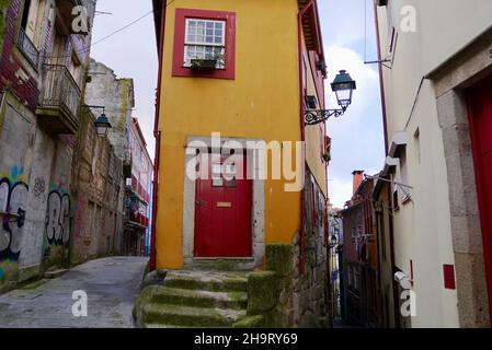 Porto, Portugal, 31.03.2017. Schmale gelbe Haus mit niedlichen roten Fenstern und Eingangstür von engen Gassen in der Altstadt von Porto, Portugal umgeben. Stockfoto