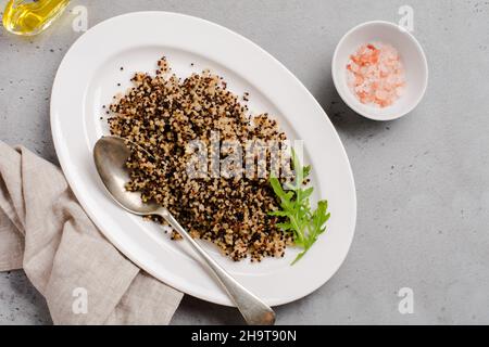 Portion gekochte Quinoa weiß, rot und schwarz in weißen Teller auf grauem rustikalem Hintergrund, Draufsicht, Platz für Textrezepte oder Menü. Vegan Superfood Stockfoto