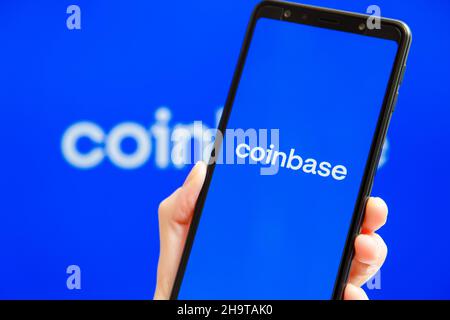 Ukraine, Odessa - Oktober, 9 2021: Hand hält Handy mit Coinbase App läuft auf dem Smartphone-Bildschirm mit Coinbase Logo im Hintergrund. Coinbase - amerikanische Kryptowährungsbörse und Handelsplattform Stockfoto