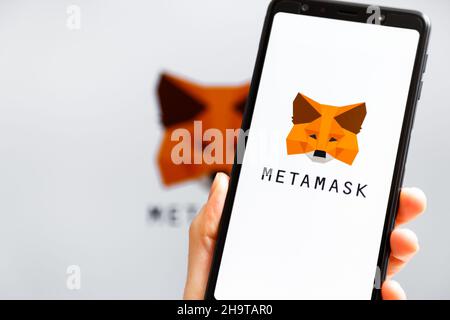 Ukraine, Odessa - Oktober, 9 2021: Hand hält Handy mit MetaMask App läuft auf dem Smartphone-Bildschirm mit MetaMask Logo im Hintergrund. MetaMask ist eine Software-Krypto-Geldbörse Stockfoto