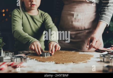 Frohe Weihnachten, Frohes neues Jahr. Lebkuchen kochen, backen. Mama und Tochter machen Kekse, schneiden verschiedene Formen von Cookies mit Metallform auf Holztisch in der Küche. Hochwertige Fotos Stockfoto