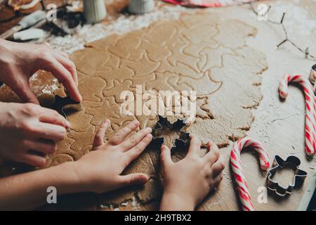 Frohe Weihnachten, Frohes neues Jahr. Lebkuchen kochen, backen. Mama und Tochter machen Kekse, schneiden verschiedene Formen von Cookies mit Metallform auf Holztisch in der Küche. Hochwertige Fotos Stockfoto