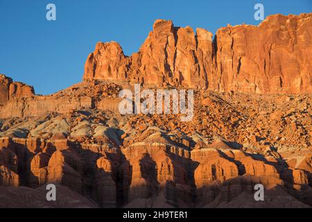 Fruita, Capitol Reef National Park, Utah, USA. Die hoch aufragenden roten Sandsteinklippen des Waterpocket Fold werden im Herbst von der untergehenden Sonne beleuchtet. Stockfoto