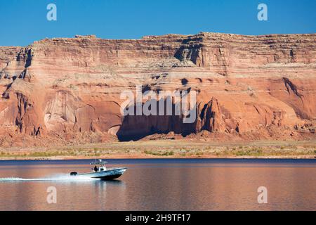 Glen Canyon National Recreation Area, Utah, USA. Kleines Boot, das über Lake Powell unter hohen roten Sandsteinklippen raste. Stockfoto