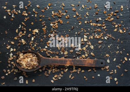 Holzlöffel voll dunkelbraunem Granulatzucker auf Schieferhintergrund aus nächster Nähe. Stockfoto