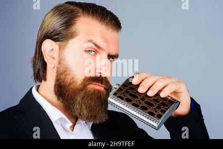 Bärtiger Mann in Anzug mit Alkohol-Flasche. Geschäftsmann mit Hüftflasche aus Metall. Alkoholgetränk. Stockfoto