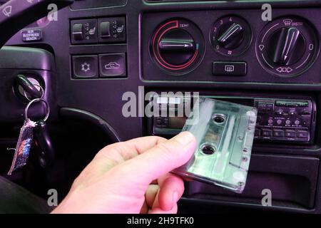 Der Fahrer legt in einem alten Auto eine Kassette in einen Kassettenrekorder ein. Stockfoto