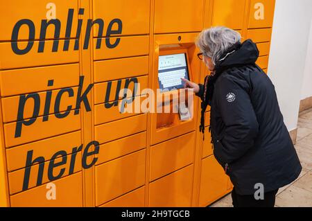 London, Vereinigtes Königreich - 04. Februar 2019: Ältere Frau, die Code am orangefarbenen Amazon (Online-Händler) Umkleidekabinen-Self-Service-Kiosk eingibt, Nahaufnahme ihres h Stockfoto