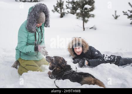 Verliebte Paare, die im Winterwald im Schnee Spaß mit dem Hund haben Stockfoto