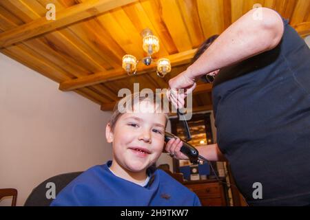 Großmutter schneidet Haare zu seinem kleinen Enkel in ihrem Hause Nähzimmer. Leben zu Hause während Lockdown. Stockfoto