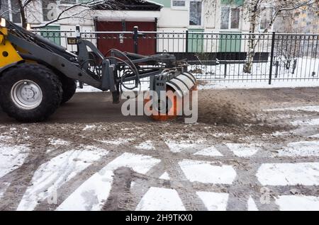 Der Traktor entfernt Schnee vom Bürgersteig und reinigt die Straßen im Winter. Sankt Petersburg, Russland Stockfoto