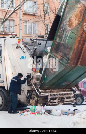 Saint-Petersburg, Russland - 27. Februar 2018: Man betreibt das Verladen von Müll von einem Straßencontainer in einen Frachtführer an einem Wintertag Stockfoto