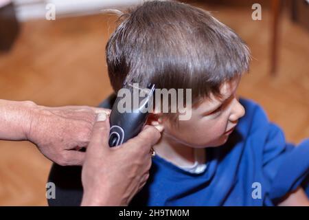 Boy hat einen Home-Haarschnitt mit einem Haarschneider zu Hause. Leben zu Hause während Lockdown. Stockfoto