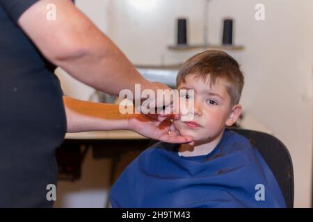 Großmutter schneidet Haare zu seinem kleinen Enkel in ihrem Hause Nähzimmer. Leben zu Hause während Lockdown. Stockfoto