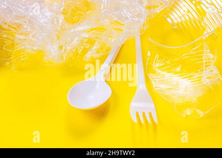 Zerquetschte Plastiklöffel, Gabeln, Flaschen und Becher als Einweg-Abfall auf hellgelbem Hintergrund. Umweltverschmutzung und Abfallrecycling concep Stockfoto