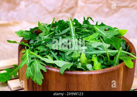 Frische grüne, würzige Rucola-Salatblätter in brauner Holzschüssel auf hellem Hintergrund. Stockfoto