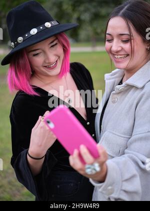 Zwei junge Frauen, die sich mit dem Telefon fotografieren, während sie lachen Stockfoto