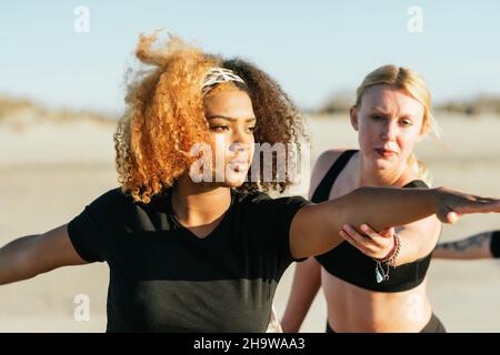 Yoga-Instuctor korrigiert die Pose einer Schwangeren während eines Kurses am Strand Stockfoto