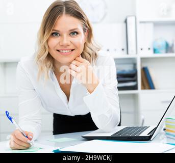 Aufmerksame Mädchen schreibt etwas auf ein Blatt Papier in modernen Büro Stockfoto