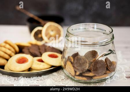 Glasglas mit Schokoladenkeksen und Teeklätzchen auf einem alten Metallteller und getrockneten Zitrusscheiben Stockfoto