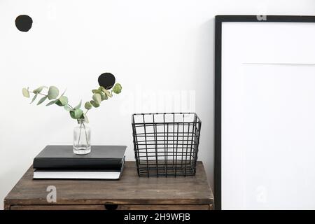 Vase mit Eukalyptuszweigen, Büchern und Korb auf Korb in der Nähe der Wand Stockfoto