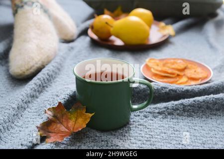 Grüne Tasse heißen Tee und abgefallenes Blatt auf grauem Stoffhintergrund, Nahaufnahme Stockfoto