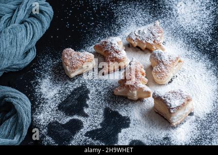 Blätterteig Weihnachtsgebäck, Baum- und Blätterteig-Herzen. Schwarze Granitplatte auf der Oberseite der dunklen Steinstruktur mit grauer Gaze-Tischdecke. Stockfoto