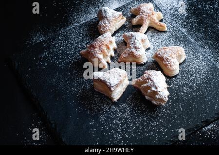 Weihnachtsplätzchen aus Blätterteig auf schwarzem Schiefergrund, bestreut mit Puderzucker Stockfoto