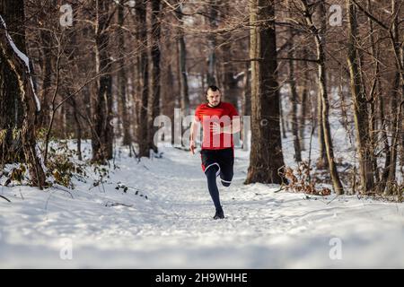 Sprinter läuft im Winter schnell im Wald auf dem Schnee. Gesunder Lebensstil, Wintersport, Outdoor-Sport, gesunde Gewohnheiten Stockfoto