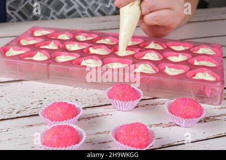 Bicho de pe, brasilianische Süßigkeiten. Im Hintergrund ein Bäcker, der Bonbons mit Ganache füllt. Stockfoto