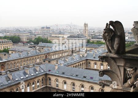 An einem regnerischen, bewölkten Frühlingstag blickt der aus Stein gemeißelte Wasserspeier aus dem Mittelalter über die Stadt Paris von der Spitze der Kathedrale Notre Dame Stockfoto