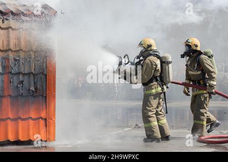 Zwei Feuerwehrleute löschen das Feuer aus dem Löschschlauch mit einem Löschwasserschaumfass mit luftmechanischem Schaum. Professioneller Urlaub Feuerwehrmann Tag Stockfoto