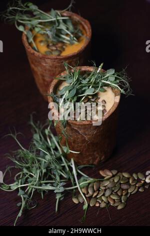 Gesunde Ernährung Konzept - zwei Tassen Suppe mit Microgreens und Kürbiskernen auf braunem Hintergrund Stockfoto