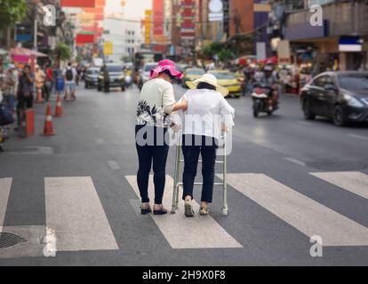 Tochter kümmert sich um ältere Frau, die die Straße in Chinatown überquert Stockfoto