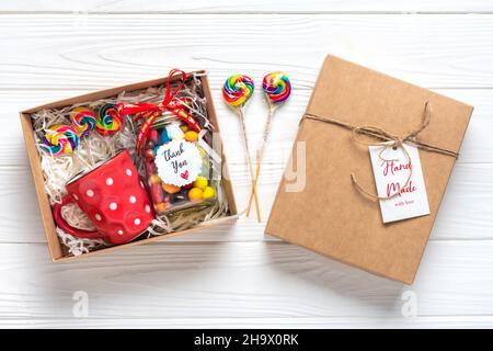 Handgemachtes Pflegepaket, saisonale Geschenkbox mit Süßigkeiten, Tasse auf weißem Tisch Personalisierter umweltfreundlicher Korb für Familie, Freunde, Mädchen für Danksagedanken Stockfoto