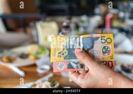 Die Hand der Frau hält australische Notizen, um im Restaurant zu bezahlen. Stockfoto