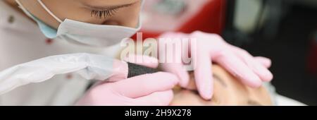 Meister in schützende medizinische Maske machen dauerhafte Augen Make-up für Kunden im Schönheitssalon Stockfoto